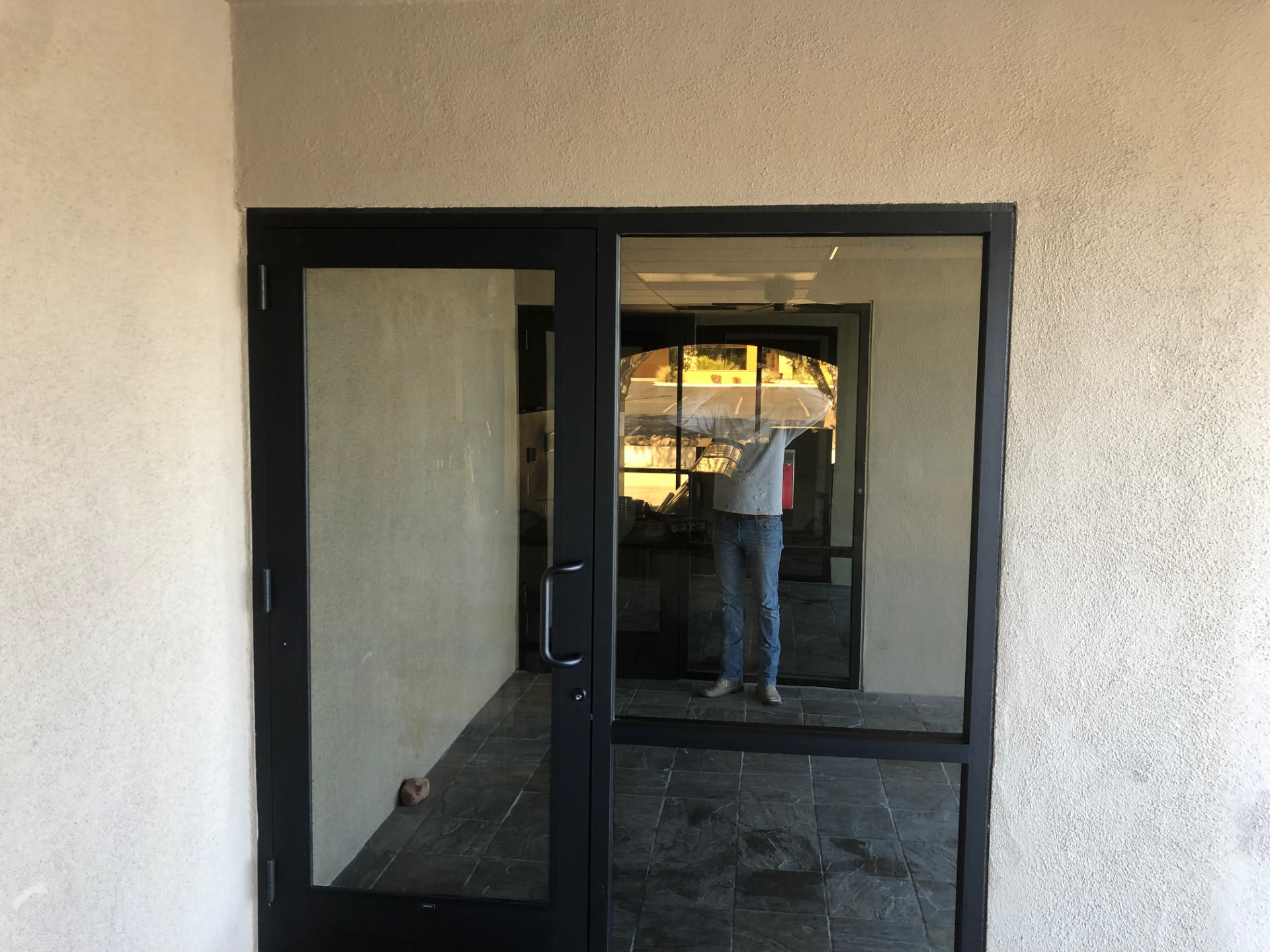 Interior office entryway with black-framed glass doors, textured walls and stone tile flooring