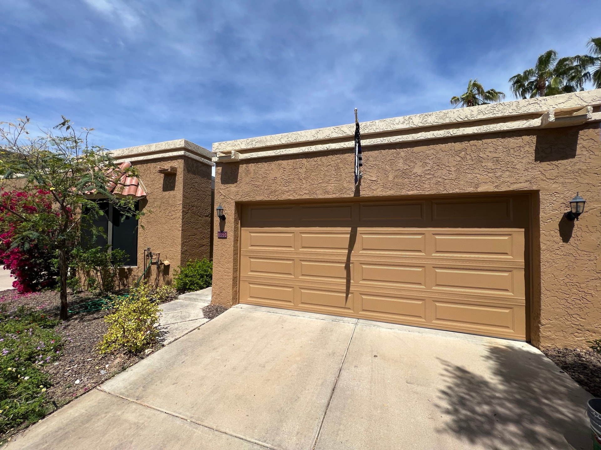 Completed exterior repaint of a stucco home with a tan garage door, painted parapet trim and stucco walls