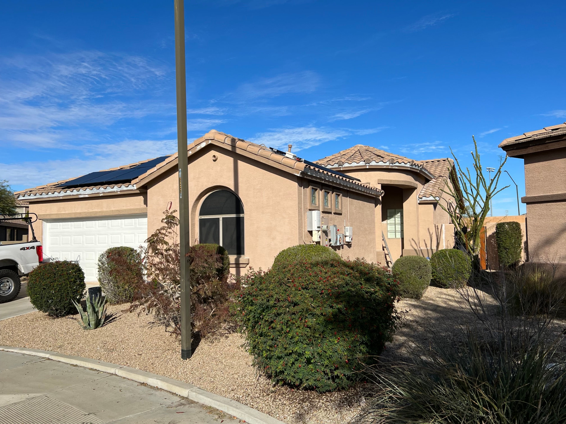 Tan stucco home exterior with solar panels, desert landscaping and a clear blue sky